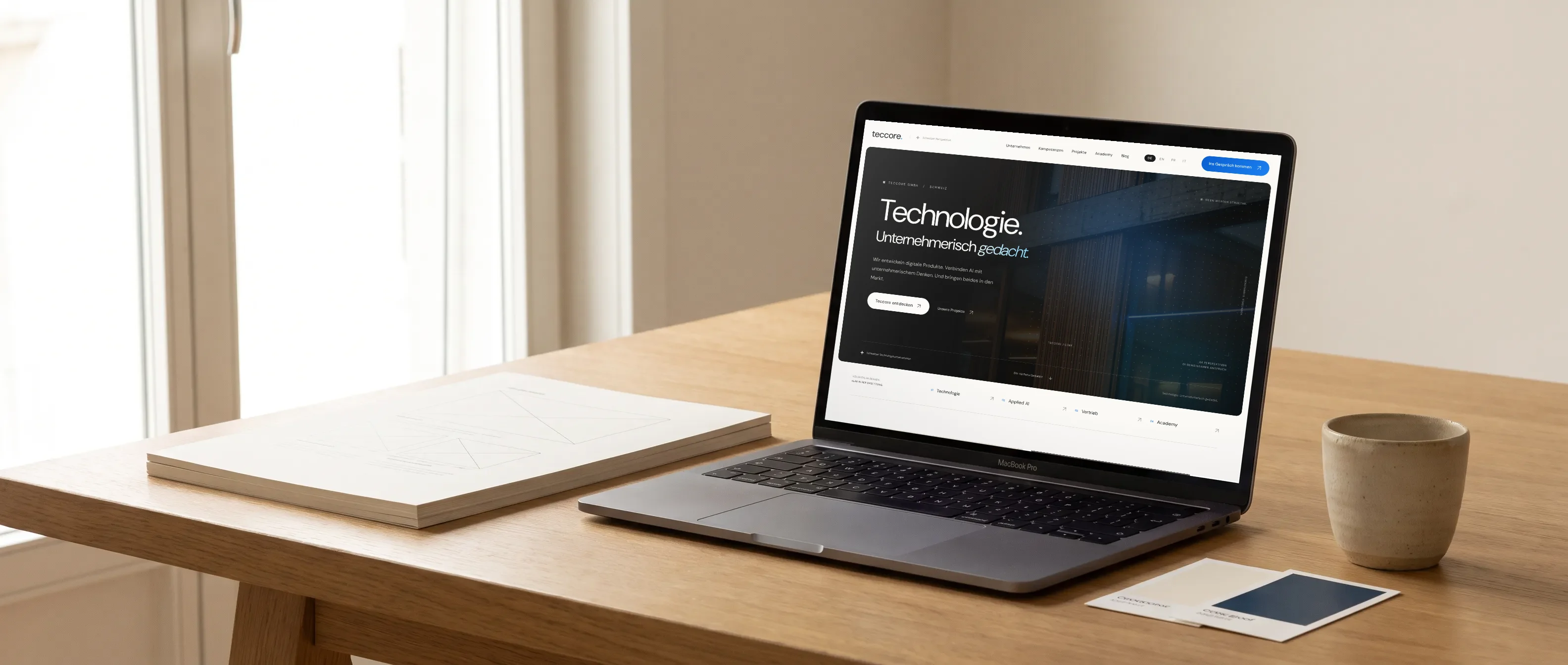 Laptop mit der Teccore-Website auf einem Holztisch, daneben Wireframe-Buch und Farbkarten